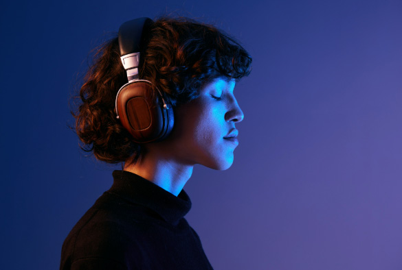 Someone listening to something in headphones with their eyes closed in front of blue background