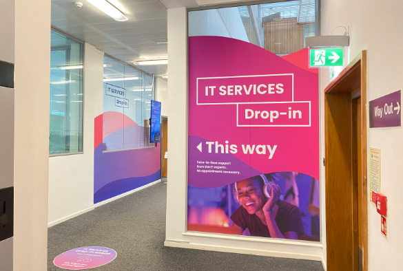 The corridor in front of the IT Services Drop-in with directional signage to the service in the foreground