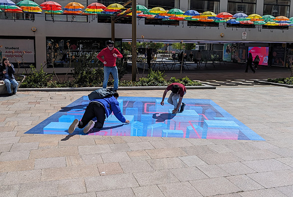 three students posing on an optical illusion installation on University Square