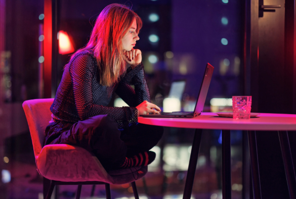 User sitting cross legged on a chair reading laptop screen under neon lighting