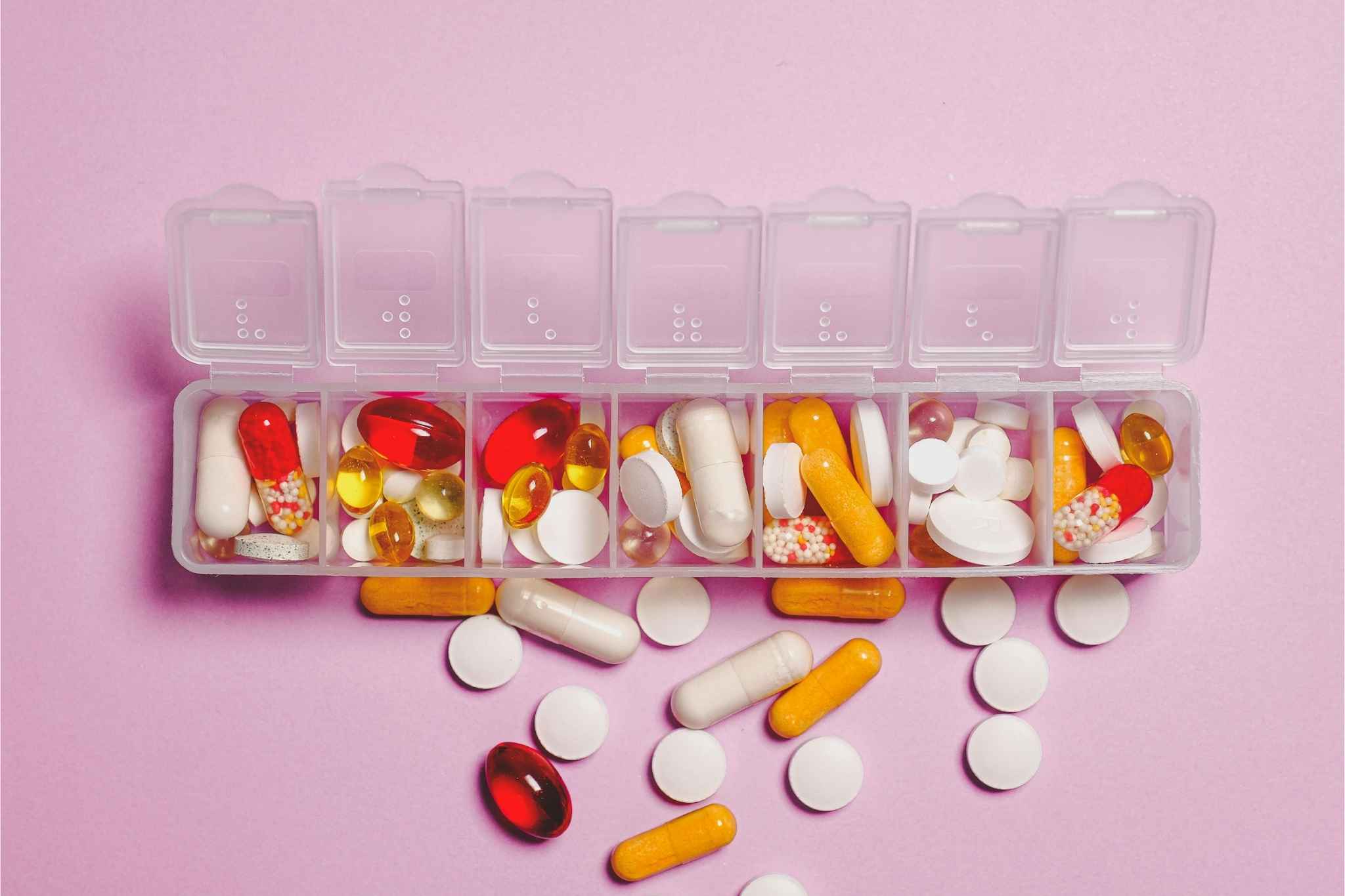 Medicine sorter containing pills on a pink background