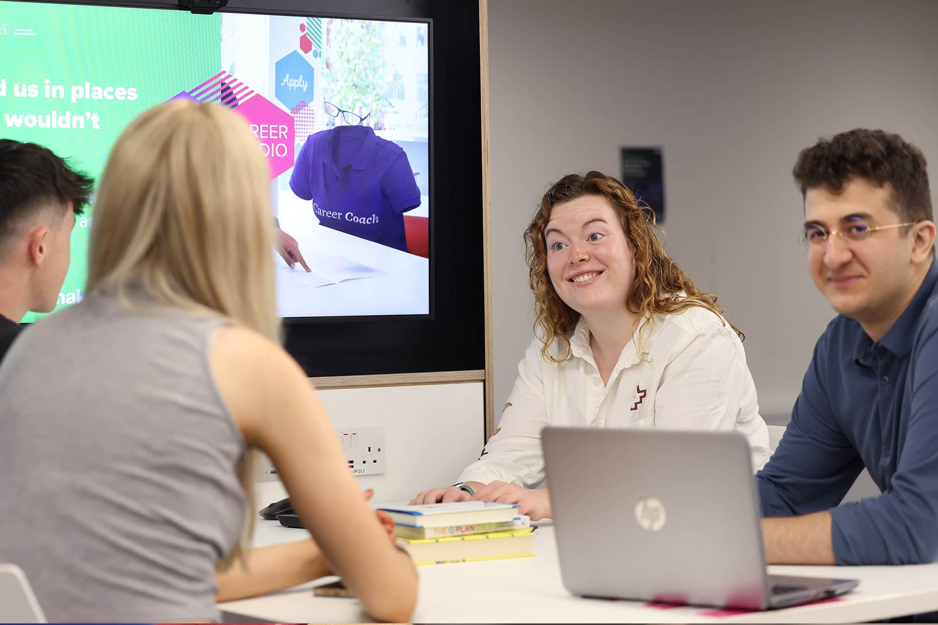 Group of students chatting at a table with laptops