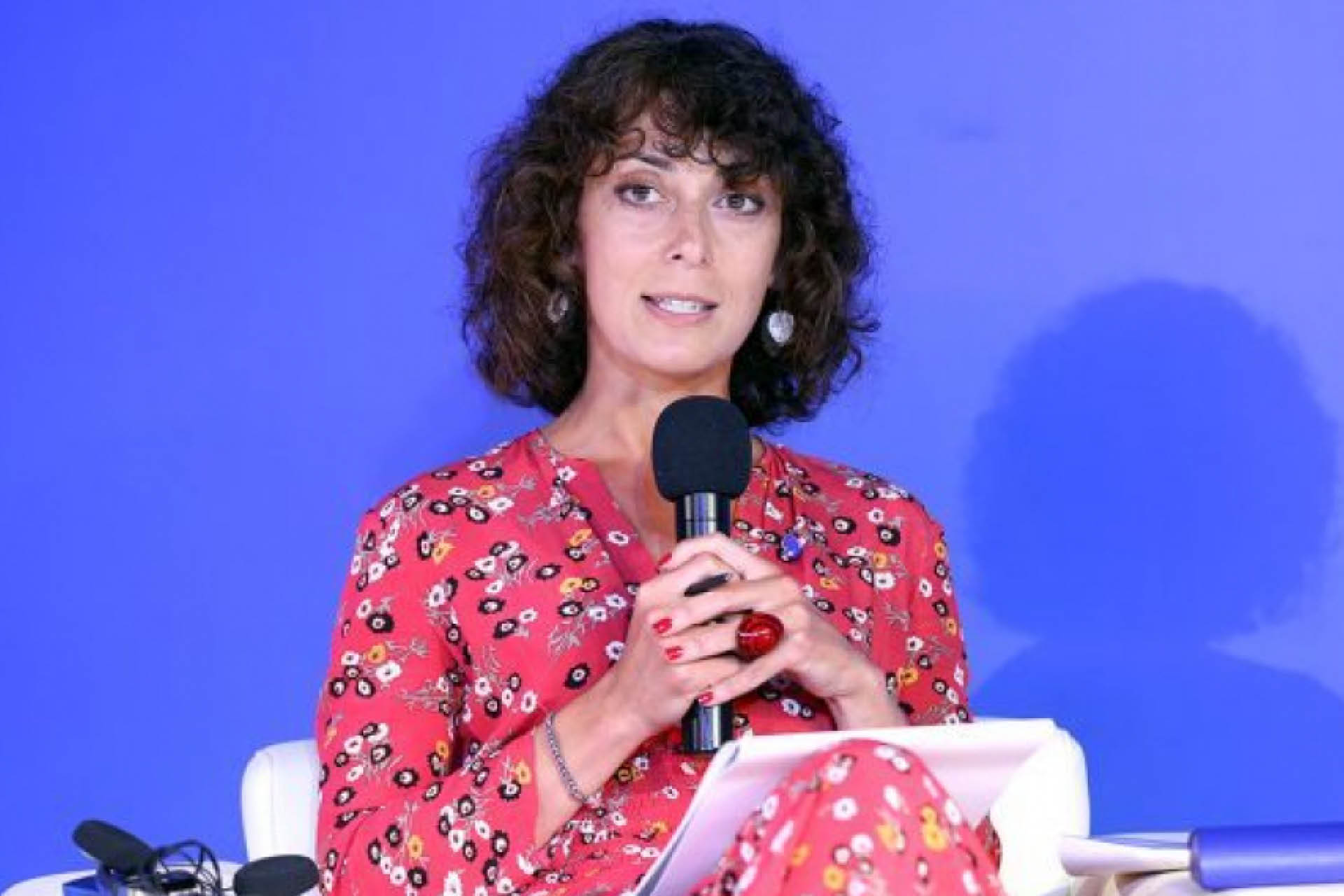 Natalie Sabanadze, a woman with short brown curly hair sits on a panel at an event and speaks into a microphone