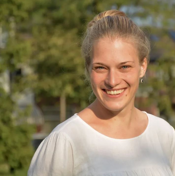 An image of Esther Kalkman, a smiling blonde woman against a background of trees