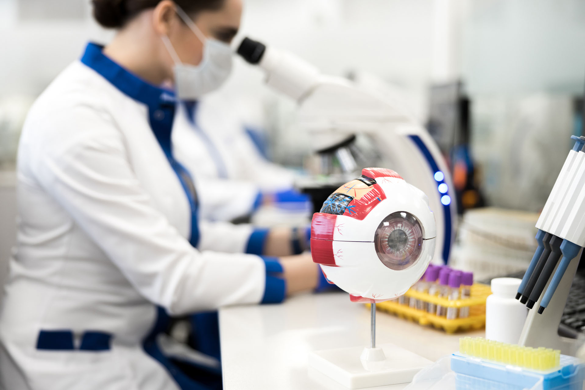 researchers working at microscope with synthetic eye in the foreground