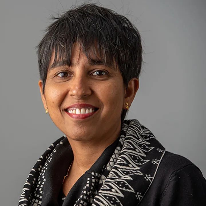 Shakila is a smiling woman with short black hair wearing a black and white scarf and black shirt.