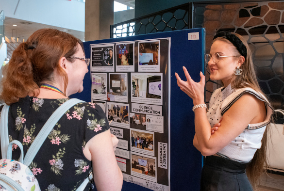 Ieva Andrulyte discussing her public engagement work with a female showcase attendee, standing in front of Ieva's poster