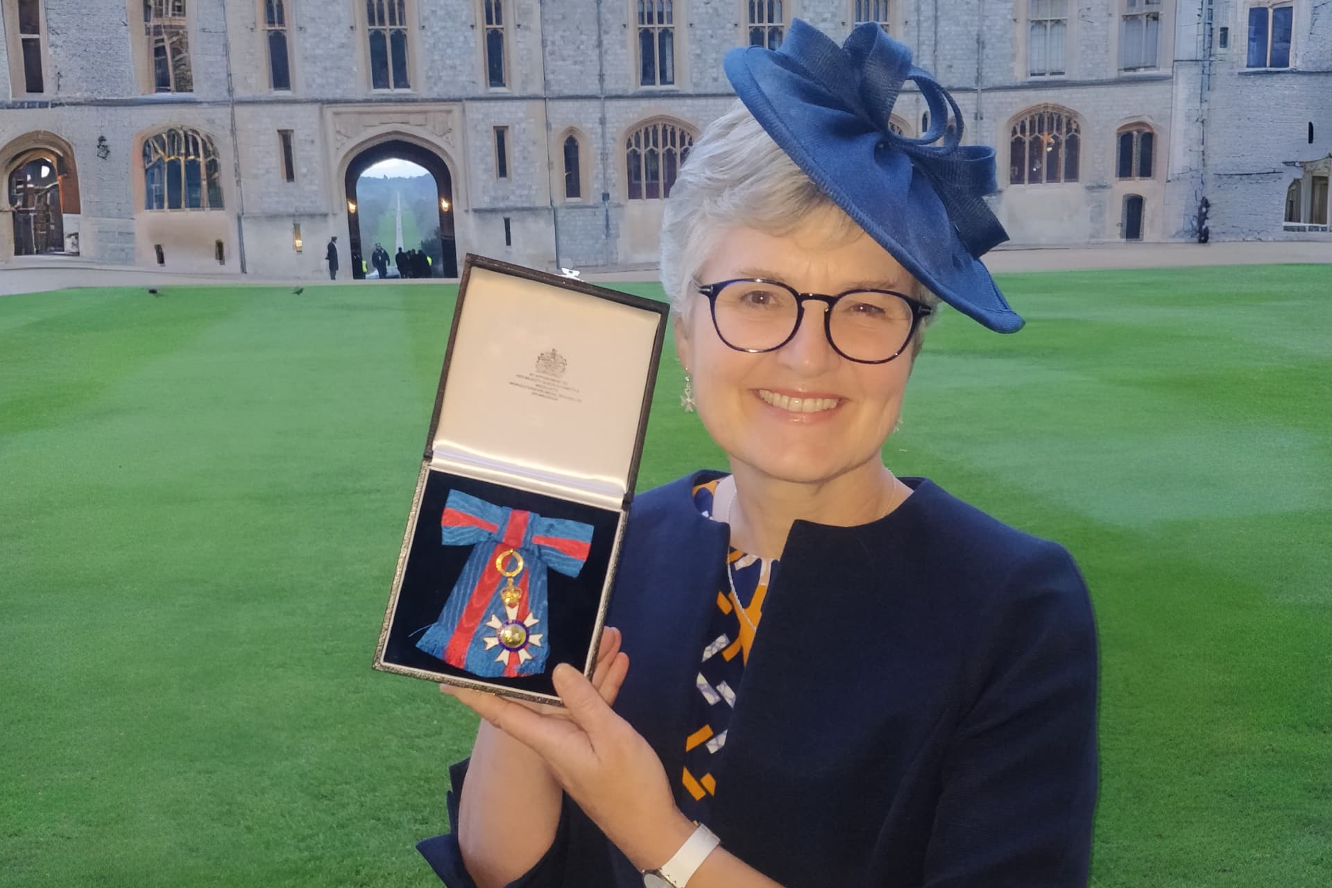 A smiling Professor Melita Gordon holding her CMG medal outside of Windsor Castle