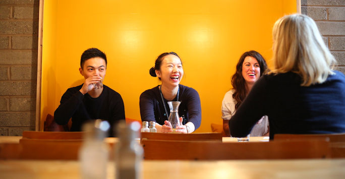 A mentoring session, with three people sat at a table, opposite one other person.