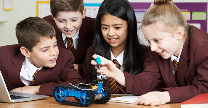 A group of school pupils beside a laptop, looking at a model of a vehicle.