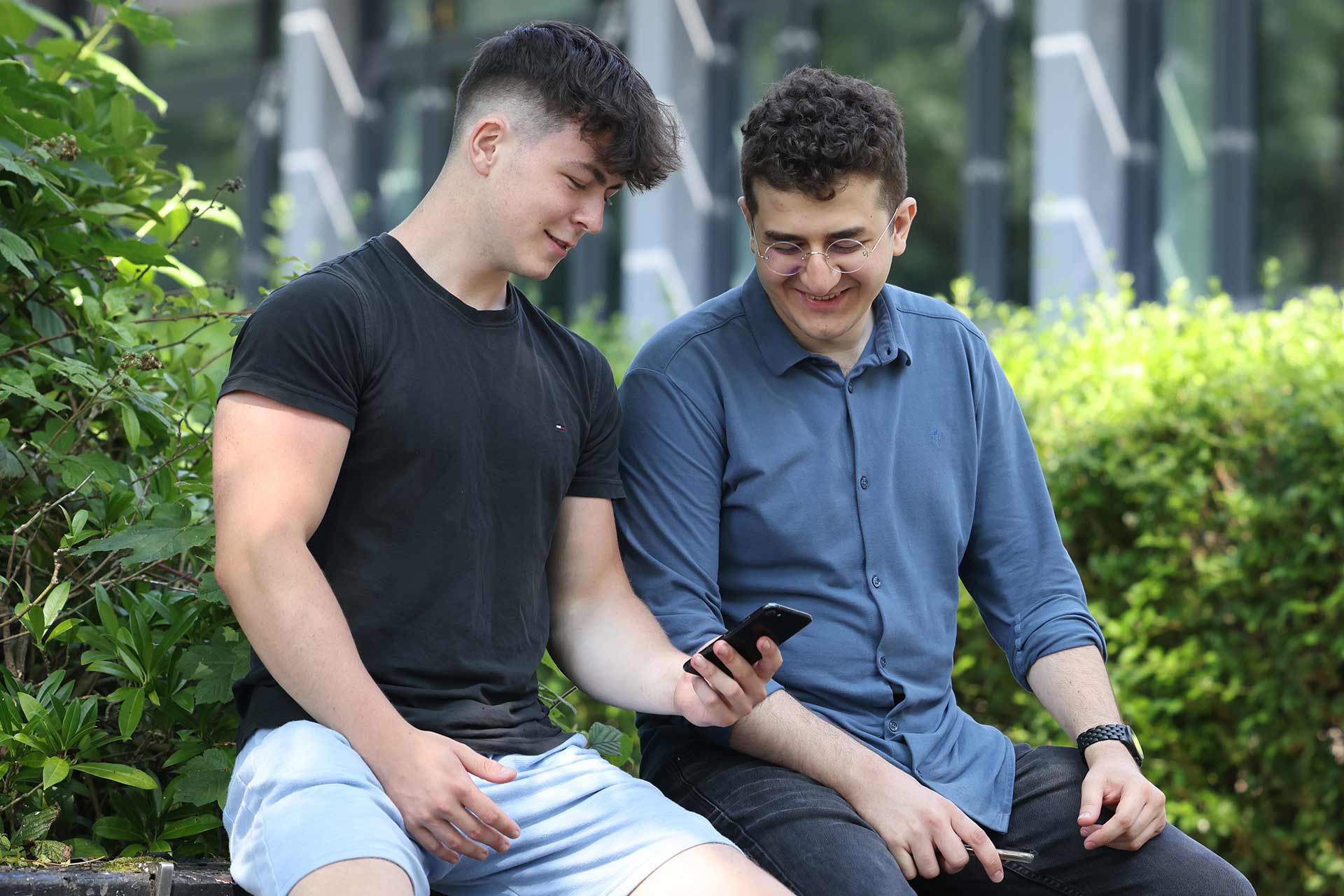 Two students sat down and looking at a phone smiling