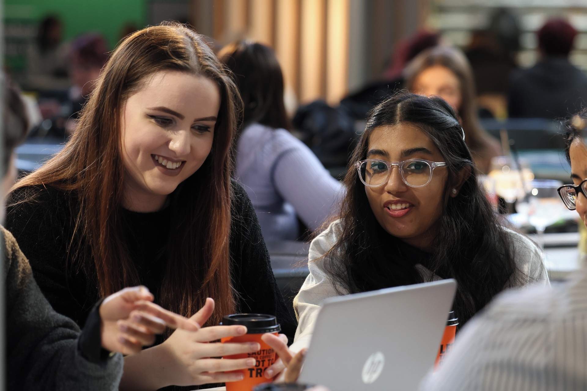 Two students on campus sitting at a coffeeshop table using a laptop