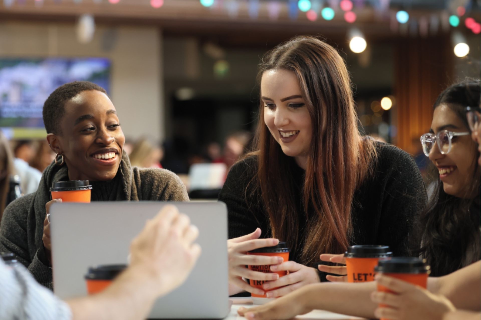 Students sit around a table with coffee cups and a laptop smiling