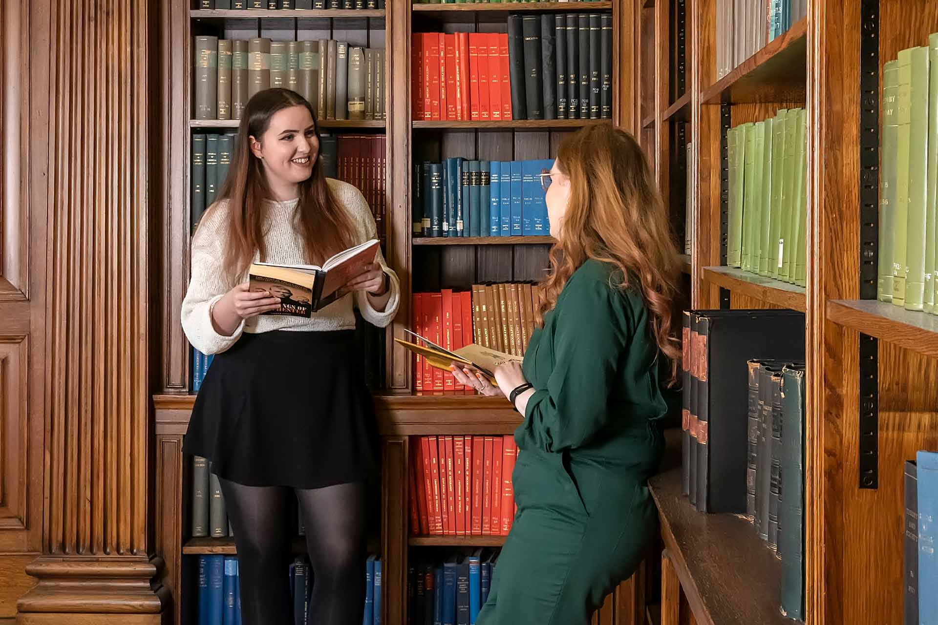 Two students stand in a library holding books