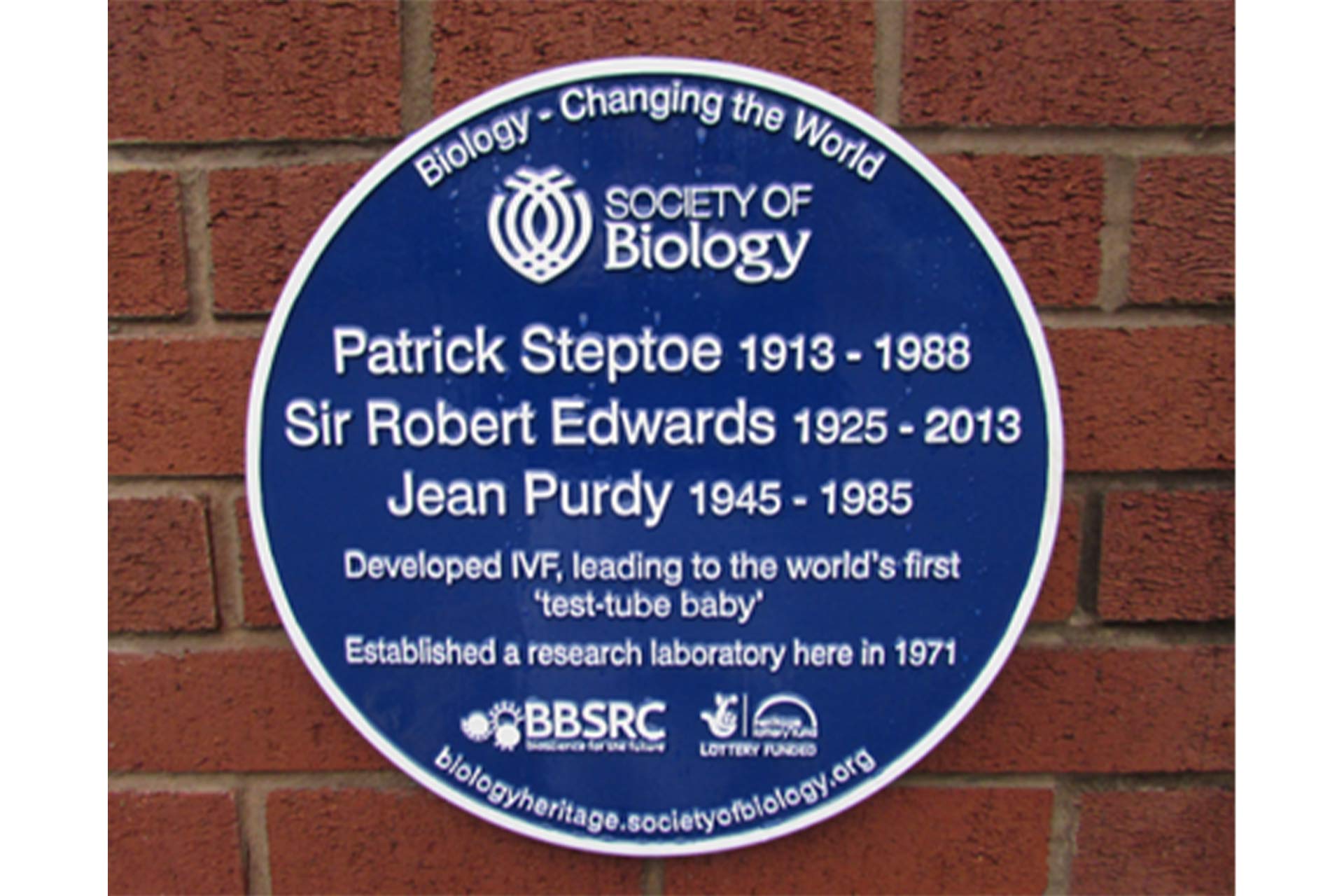 A blue plaque on a brick wall with the names Patrick Steptoe, Sir Robert Edwards and Jean Purdy on with 