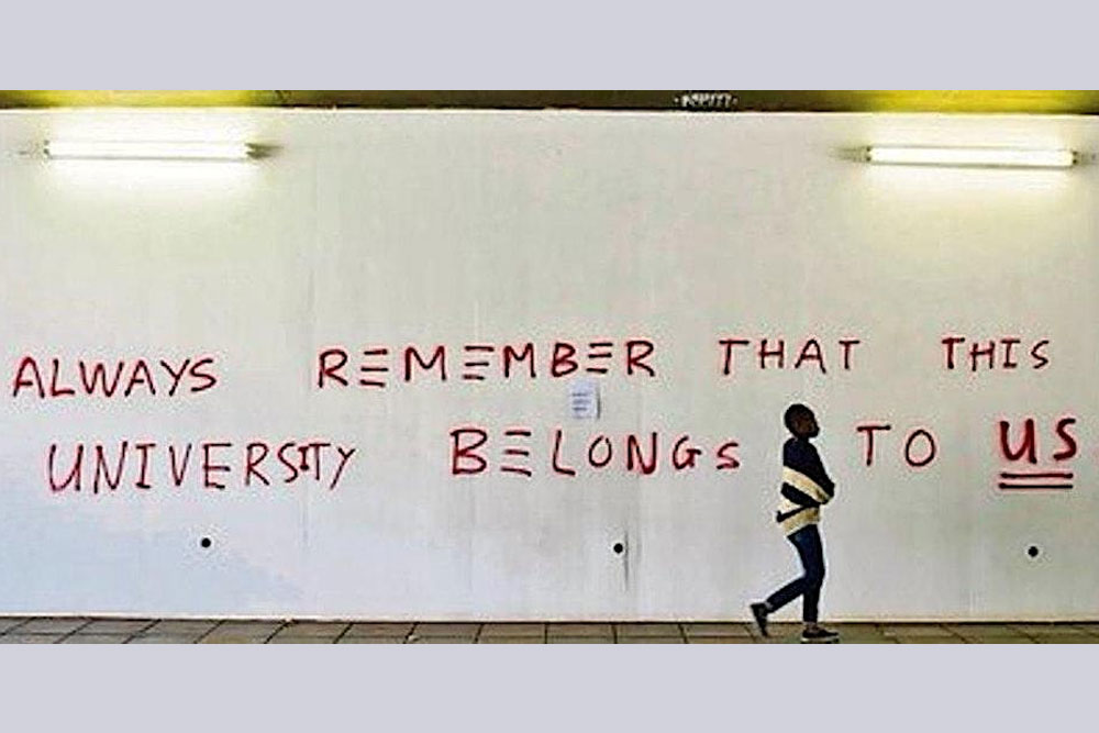 A woman walking past a wall with 'Always remember that this university belongs to us' written on it.