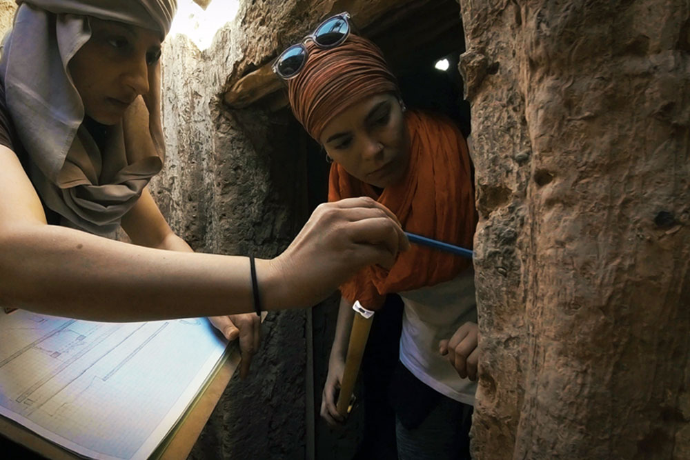 Two archaeologists working on a sandstone wall.