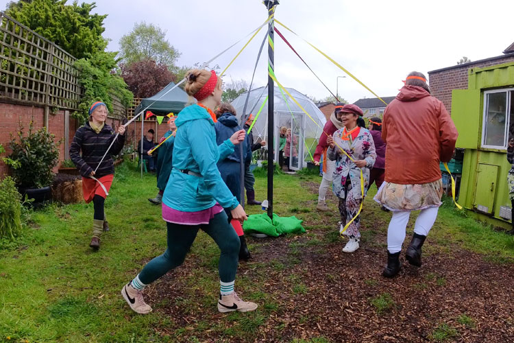 Women dancing around a small maypole in a garden