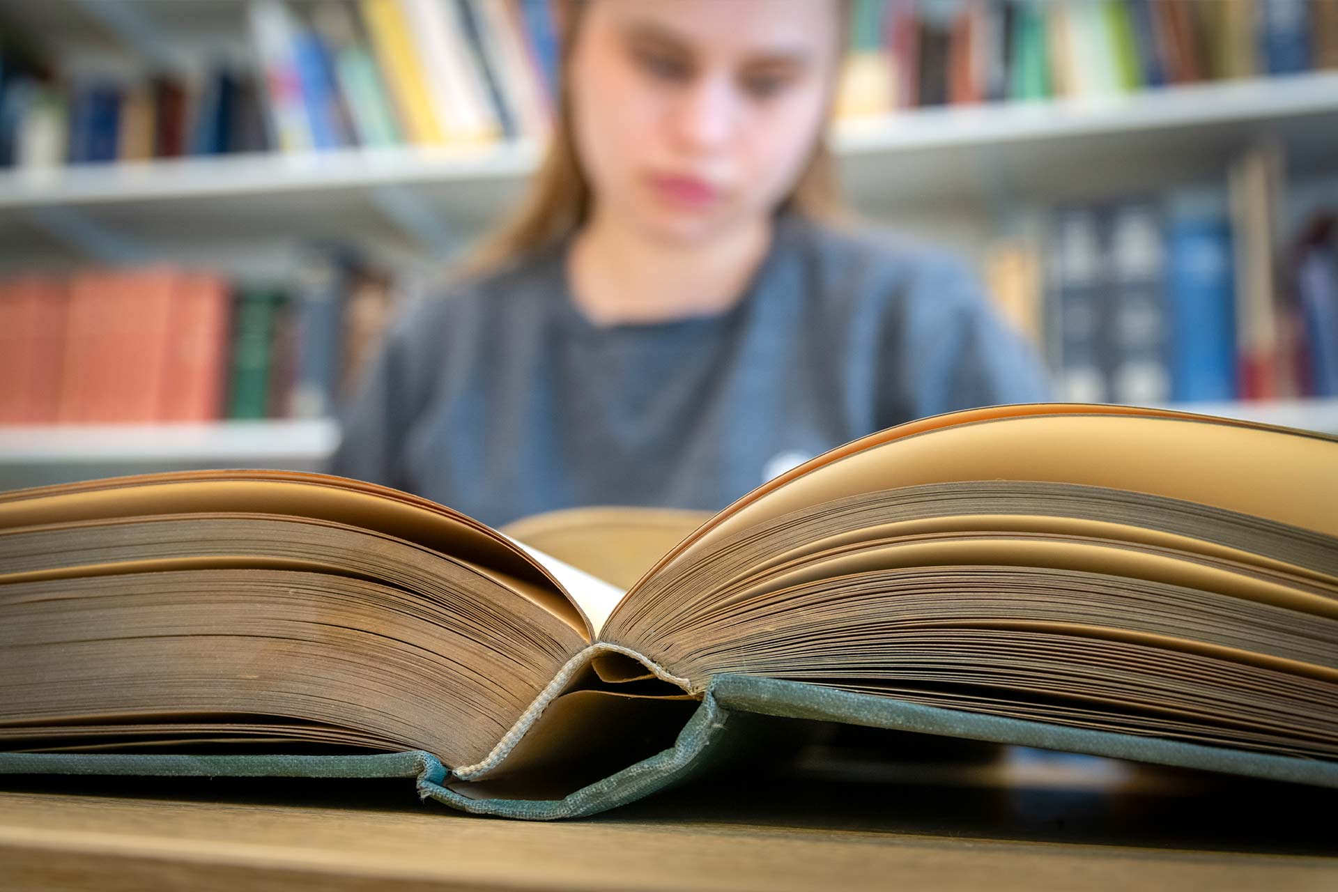 Close up of an open book, a girl reads in the background