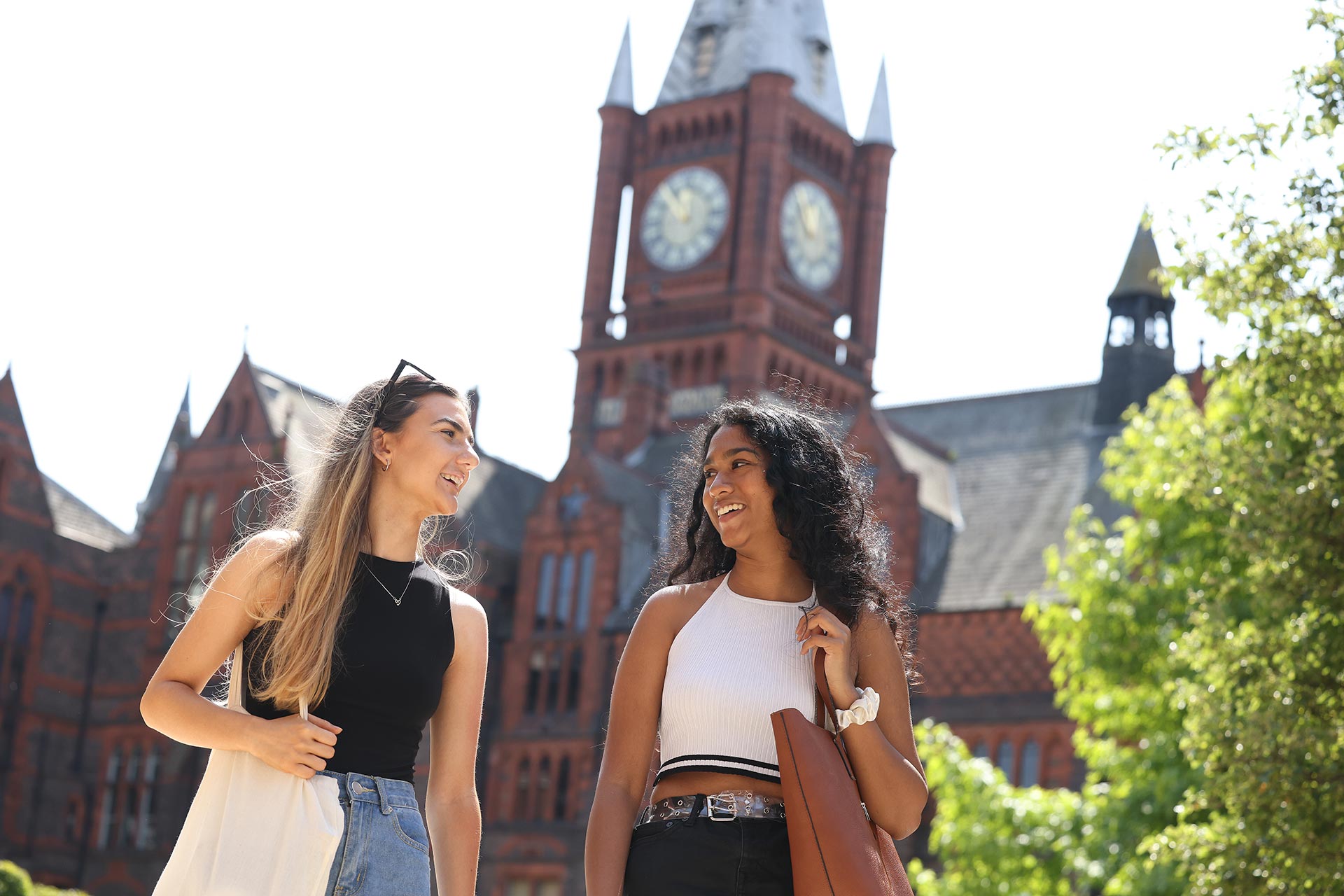 Two female students walking through campus in front of the VGM smiling at each other