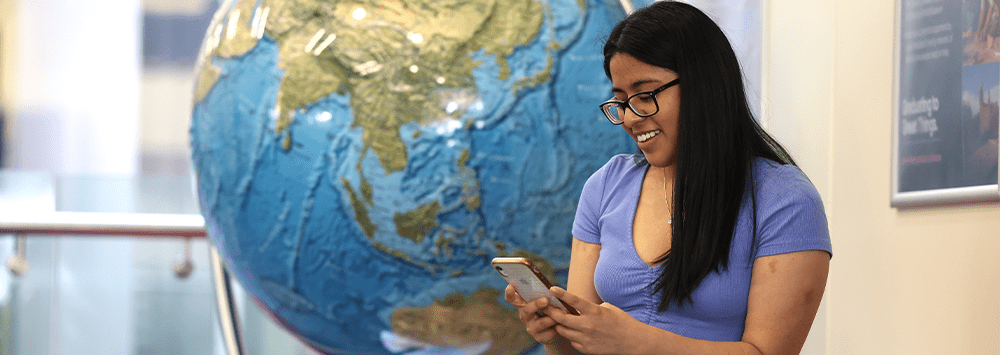 A student is on her phone, a globe is behind her