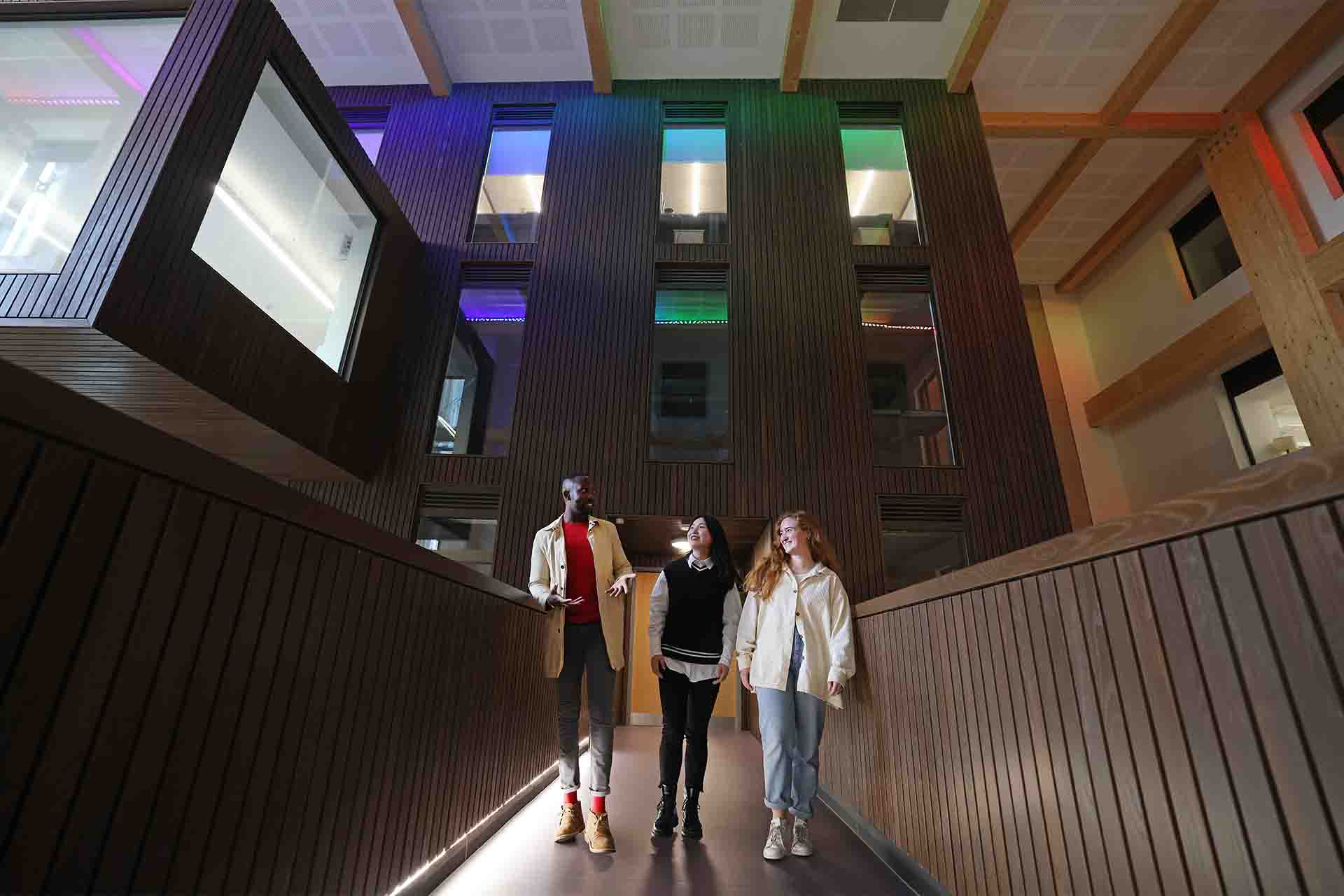 Three students walking across a bridge in School of Law and Social Justice building.