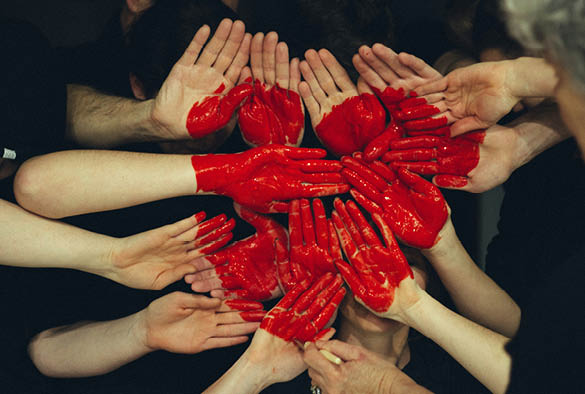 A collection of hands with a red heart painted in the middle.