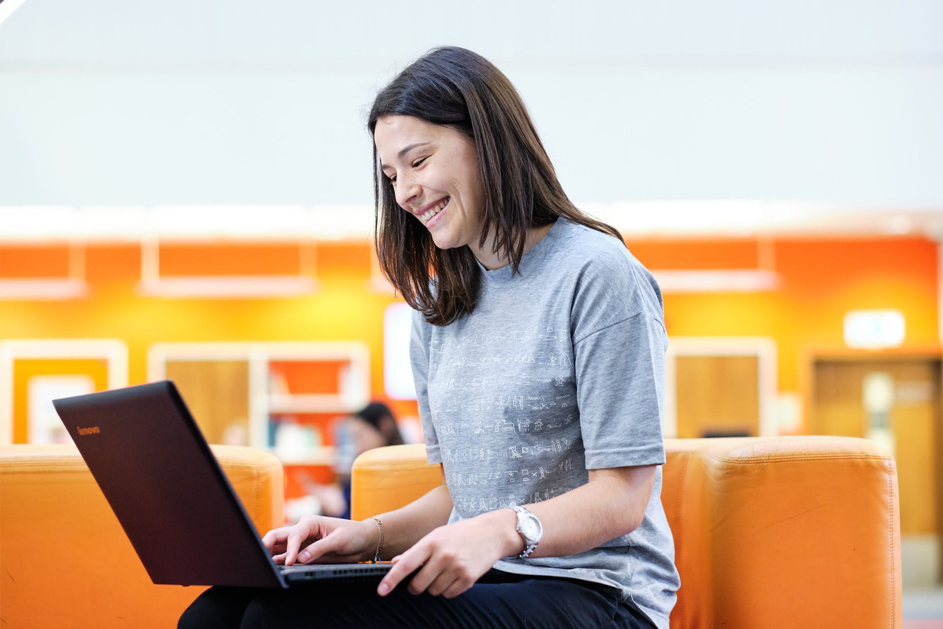 A student sits with a laptop on her knee, focused on the screen.