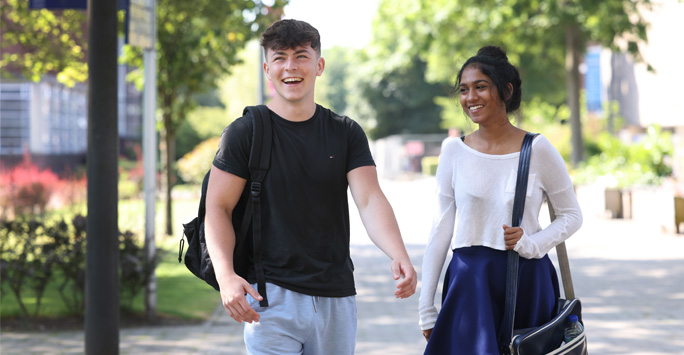 Two students walking through campus together on a sunny day.