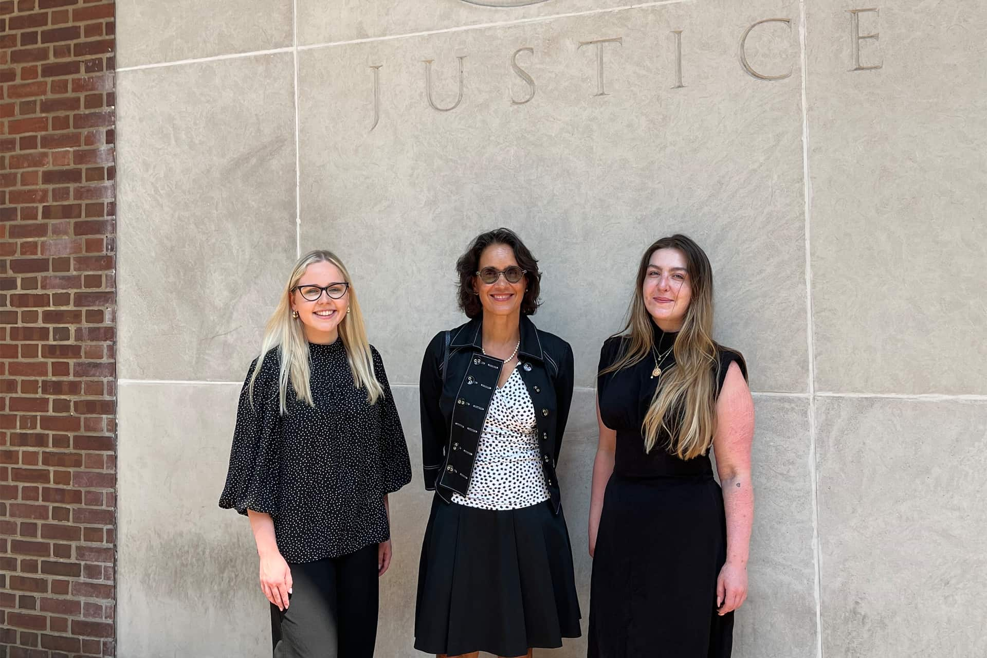 Elizabeth stands against a wall with Judge Beetlestone and another student on the internship.