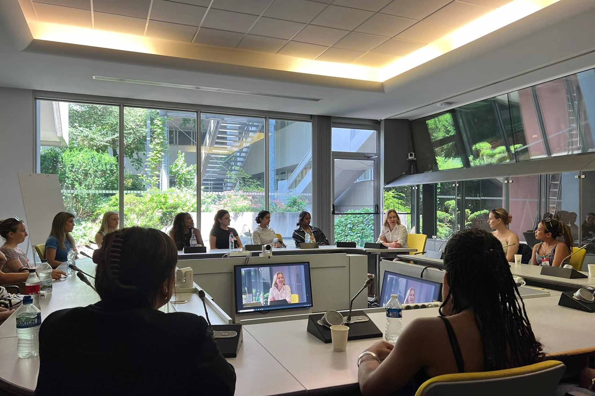 Students sit at desks and screens listening to a talk.