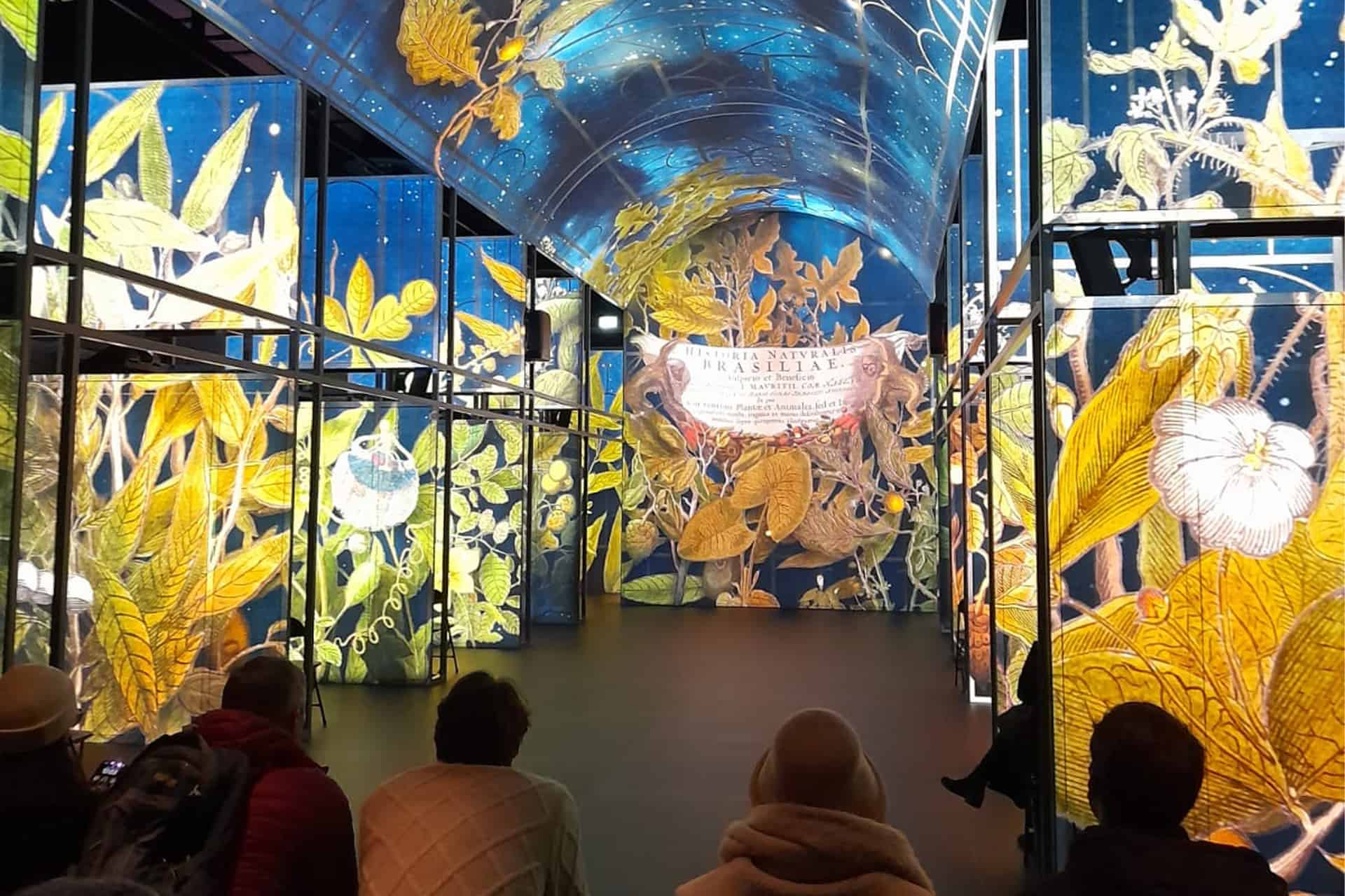 People sit in a bench in a room a large filled with a light installation on the walls and ceiling.