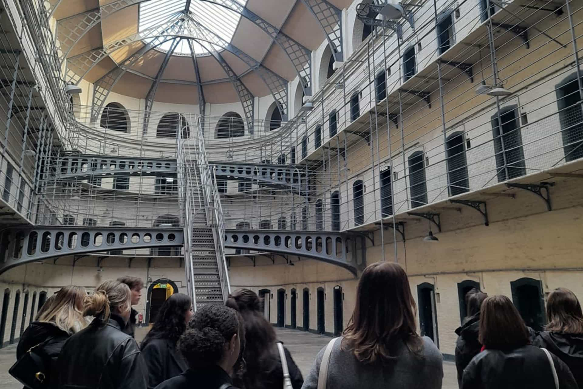 A group of students stand inside a prison. There are many floors filled with cells.