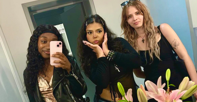 Three students pose together for a selfie in a large bathroom mirror.