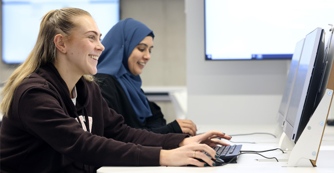 Two students work on computers on a desk.