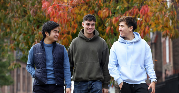 Three students walking through campus on an autumn day.