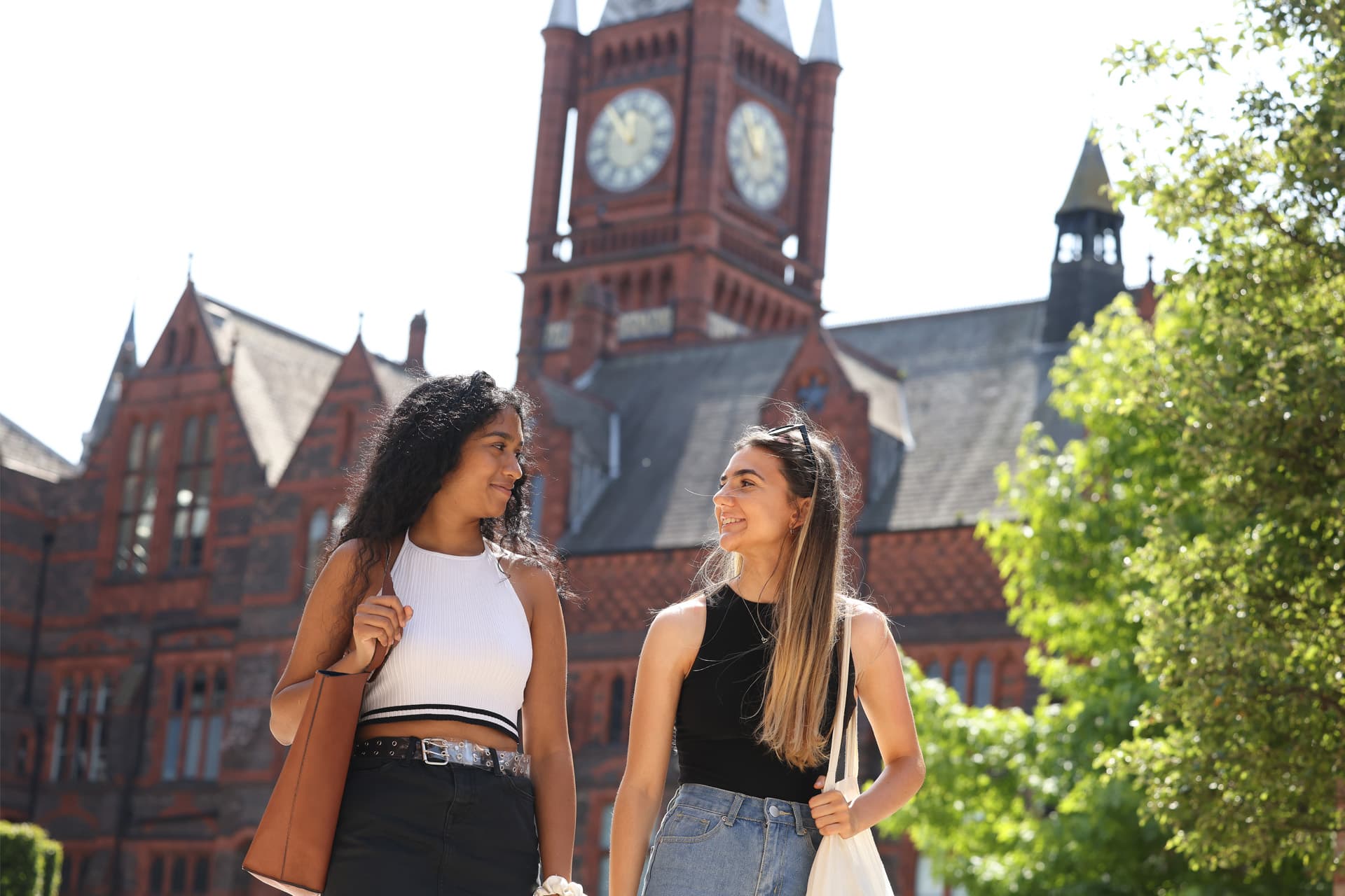 Two students walk together in front of a large redbrick building.