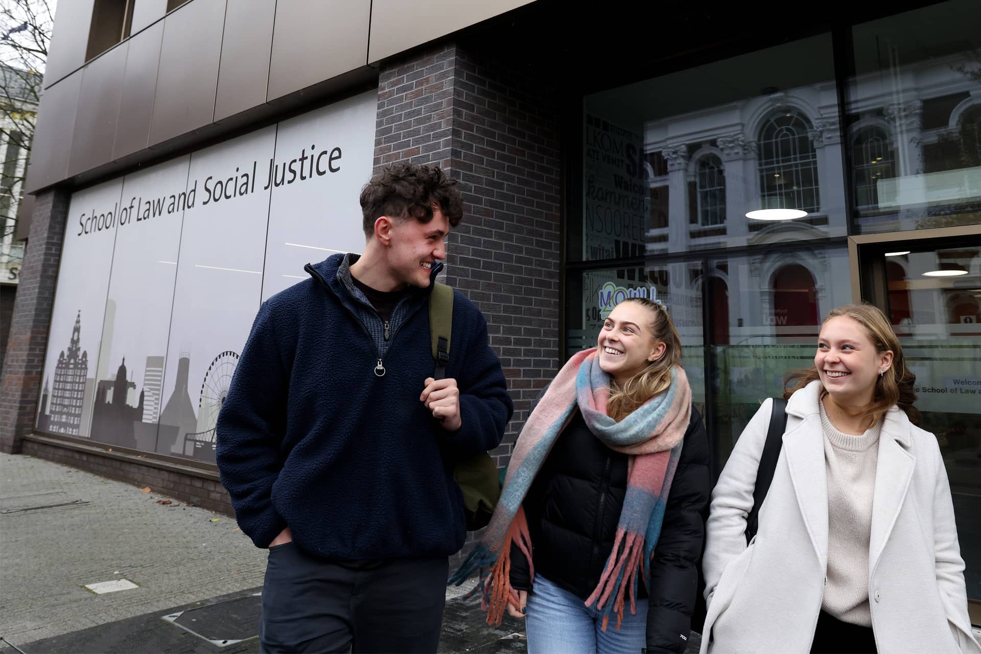 2/2 ChatGPT said:  Three students walk together, smiling at each other, in front of a building with a window sign that reads 