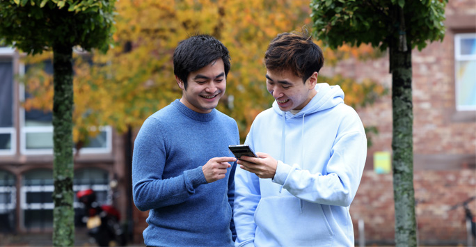 Two students look at a phone that one of them is holding.