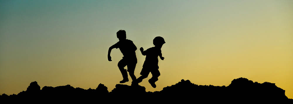 Two silhouettes of children jumping at sunset.