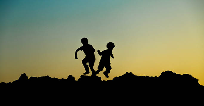 Two silhouettes of children jumping at sunset.
