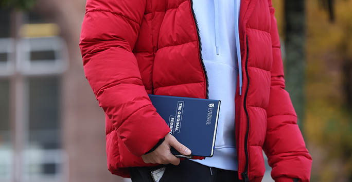 Someone walking carrying a University of Liverpool notebook