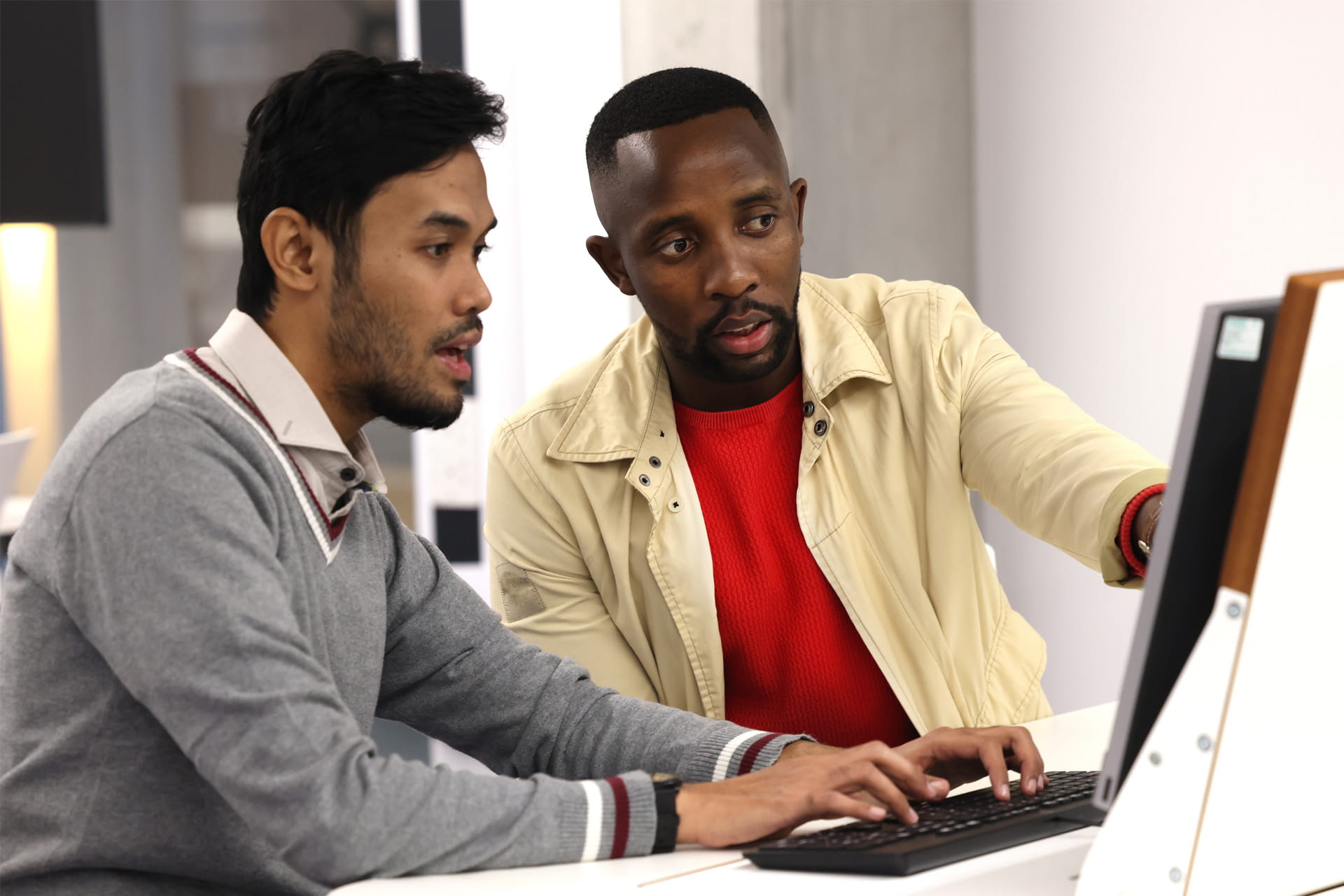 Two students sit closely together at a computer, focused on the screen, collaborating on a task.