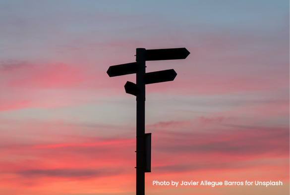 A sign post in the shadow of a sunset sky.