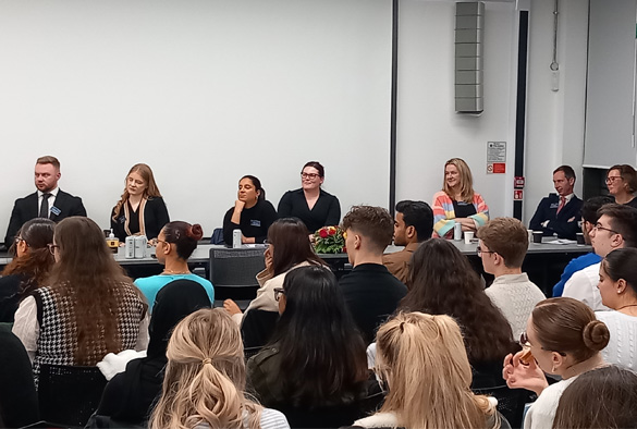 A panel of speakers sits at the front of the room, facing an audience.