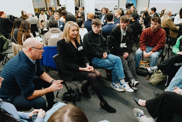 A room filled with seated students in conversation with visiting legal professionals.