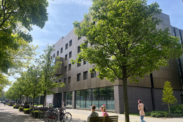 The front exterior of the School of Law and Socila Justice Building. In front of the building are trees, students, benches and bikes.