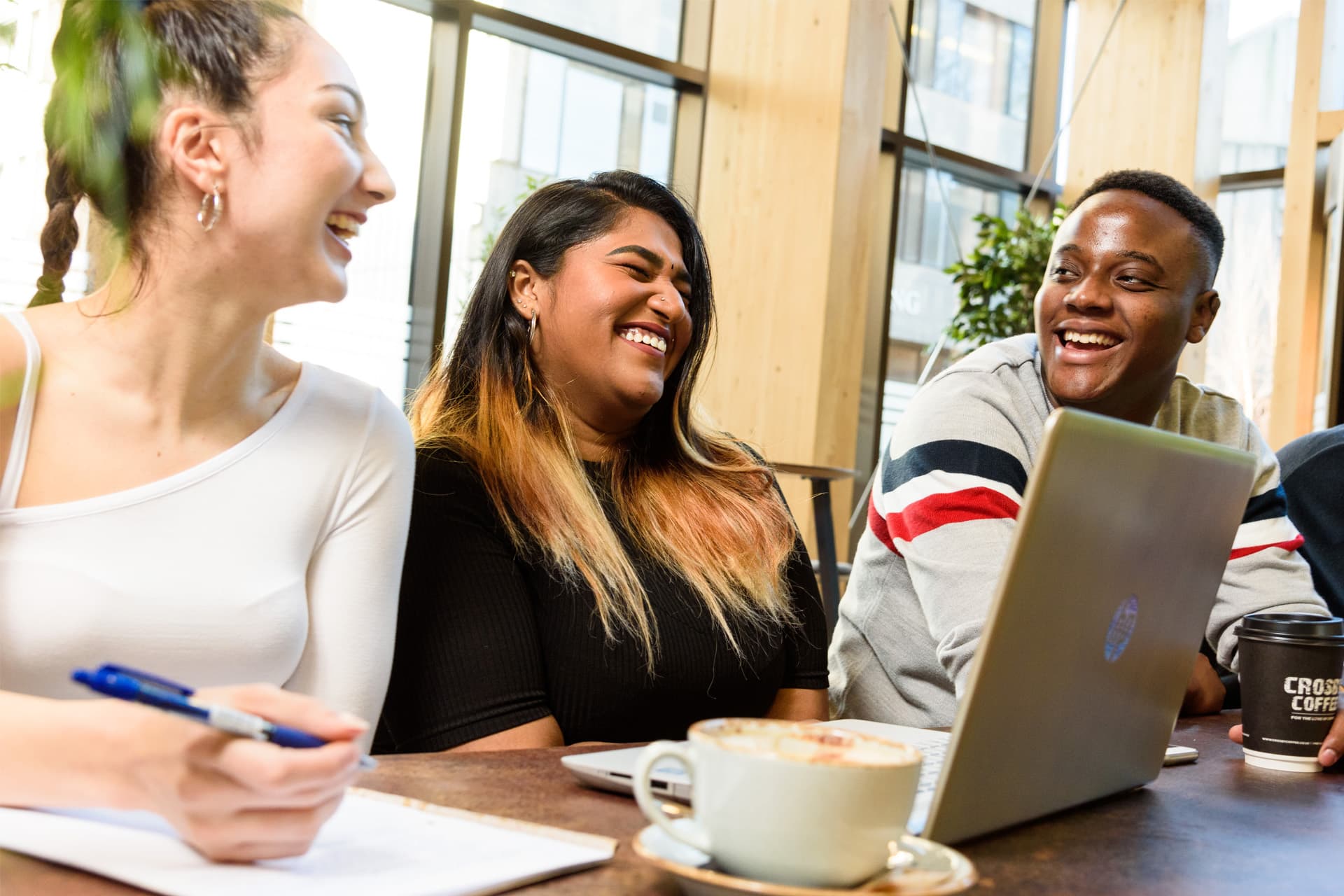 Three students sit together at a table, smiling and laughing while engaged in conversation.