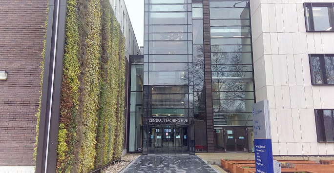 Exterior of the Central Teaching Hub: A glass front building with a  wall to the left of the building is a living wall covered in plants.