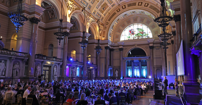 A large hall filled with people sat on circular tables.